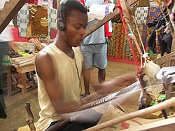 A man weaves Akan Kente cloth using a traditional loom while listening to music, Bonwire village, Ejisu-Juaben Municipal District, Ashanti Region, Ghana.