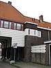 Poortgebouw met twee winkels met bovenwoningen, met veel hout zoals de zware kolommen in poort, bouwstijl Amsterdamse School, ligging aan Purmerweg centraal deel van Tuindorp Nieuwendam