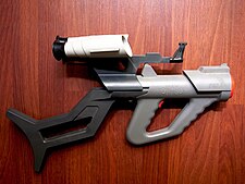 Plastic, gray toy gun with orange highlights and attached black shoulder stock and white scopes