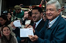 Lopez Obrador (right) holding his Voter ID upside down along with Marti Batres (center) after submitting the formal political registration of MORENA to the INE AMLO se afilia a MORENA en el Zocalo (8361522287).jpg