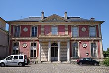 Au premier plan, la cour pavée ; la Folie est au deuxième plan, éclairée par le Soleil. Façade rose avec avant-corps central.