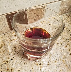 На мраморной столешнице стоит стаканчик с прозрачной коричневой жидкостью.