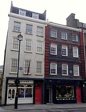 A color photograph of two adjacent buildings, the one on the left is white and the on the right is dark brown.