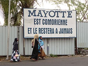 La devise sous l'écu, « Ra Hachiri » (« Nous sommes vigilants ») vient des revendications des Comores sur Mayotte (ici sur un panneau à Moroni[17]).