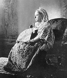 Photograph of a seated woman in embroidered and lace dress staring into the distance, looking sad