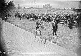Cycliste posant sur son vélo, un bouquet à la main, sur la piste d'un vélodrome.