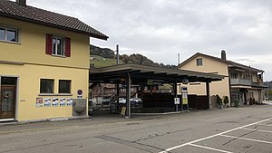 Two-story station building with gabled roof next to canopy-covered waiting area