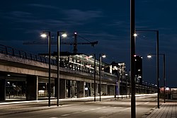 Et nattlig syn på en viadukt langs med veien. I midten av bildet er en stasjon i glass.