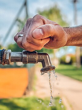 Hand turning on a public water faucet next to a playground