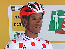 Photo portrait couleur d'un cycliste noir africain portant un casque rouge et blanc et le maillot blanc à pois rouges de meilleur grimpeur.
