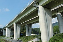 橋脚の天端を高く構築することで沓（支承）を隠し、雨水による汚れを目立たなくさせた。左画像は伊勢湾岸自動車道の高架橋で沓が露出することで橋脚が汚れているが、右画像の藁科川橋では沓を隠して汚れが目立たない[397]。