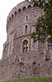 Фотография с левой стороны круглой каменной башни из серого камня с небольшими окнами.