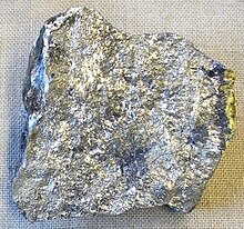 An irregular piece of silvery stone with spots of variation in luster and shade.