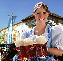 Garçonete com canecas de cerveja da marca Hacker-Pschorr, uma das cervejas tradicionais servidas na Oktoberfest. Ela usa um Dirndl, um vestido tradicional da Baviera. A Oktoberfest, em Munique, é um dos maiores festivais folclóricos do mundo. É realizada anualmente no Theresienwiese, na capital da Baviera, desde 1810 (com cancelamentos devido a guerras ou pandemias) e é um importante fator econômico para a cidade. A data é de meados de setembro ao início de outubro. As canecas de cerveja utilizadas nas tendas dos festivais não são mais feitas de cerâmica, mas de vidro, para pelo menos dificultar as fraudes. Elas são propriedade das respectivas cervejarias. (definição 3 961 × 3 870)