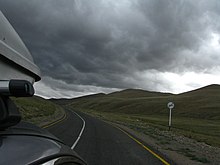 Photographie prise depuis le haut d'une voiture montrant ce qui se passe derrière la voiture. En l'occurrence, l'on voit la route ainsi qu'un nuage très gris, soit un orage qui se prépare.
