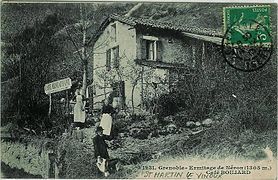 Old postcard with a man and two women wearing aprons in front of a café-restaurant.