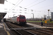 Un train de voyageurs est en gare. On peut voir au loin les voies de garage pour les trains de marchandises.