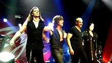 Quatre membres d'un groupe habillés de noir saluent son public à la fin d'un concert