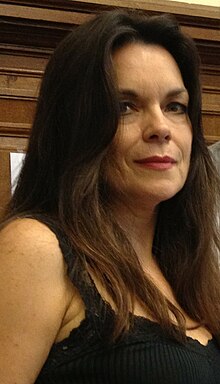 Upper body shot of a woman. She has dark hair which is worn loose, and is wearing a dark top.