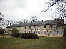 Photographie du bâtiment principal de la Colonie, à Condé-sur-Vesgre. Il s'agit d'un long bâtiment symétrique à un étage, avec des grandes fenêtres régulières, six de chaque côté de la porte. Devant, un petit terrain pelousé avec des buissons et quelques arbres.