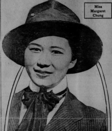 Schwarz-Weiß-Porträt von Margaret Chung. Sie trägt einen schwarzen Hut, ein weißes Hemd, ein schwarzes Jackett mit weißen Streifen und eine kurze schwarze Krawatte.