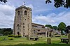 A stone church with a west tower, and a body of complex design including a porch and large rectangular paned windows in the clerestory.