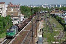 Vue d'un train de fret passant au droit du bâtiment voyageurs de la gare.