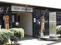 Entrance to a mult-storey building. There is a wood statue with an anthropomorphic head at each side of the door.