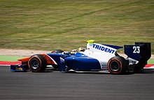 Photographie d'une monoplace de GP2, bleu foncé, blanche et orange, vue de profil.