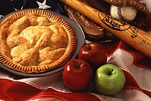 Posés sur un drapeau américain une tourte, trois pommes, une batte, un gant et une balle de base-ball.