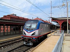 A gray electric locomotive with a blue roof and a thin red sill stripe. The cab window is surrounded by black and blue areas, with a red stripe at the bottom.