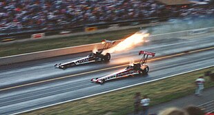 Drag racing is a sport in which specially-built vehicles compete to be the fastest to accelerate from a standing start. DonPrudhommeFire1991KennyBernstein.jpg