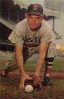 A man in a white baseball uniform and navy blue cap