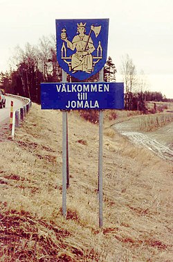 "Welcome to Jomala." The coat of arms of Jomala features St. Olav sitting on a throne and holding an axe and a globus cruciger