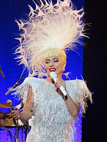Lady Gaga on stage in a white dress and feathery headpiece