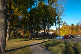 Tree-lined path to parking lot, with red-and-gray building in background