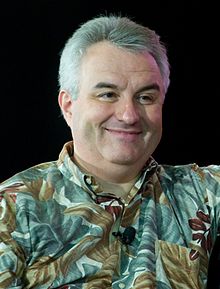 Photograph of Leo Laporte's head and shoulders. Leo is pictured wearing a patterned shirt. There is a black background and Leo is smiling.