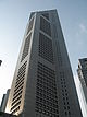 Ground-level view of 60-storey building whose cross section is a square with a diagonal projection from one corner. In the top 10 storeys part of the square is missing and only a diagonal remains.