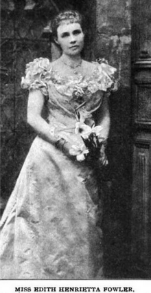 A young white woman, standing, wearing a gown with a ruffled neckline and holding lilies