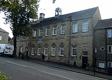 A two-storey white building with grey window frames, several cars are parked in the foreground.