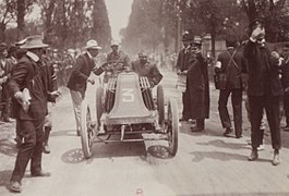 Photographie d'une voiture à l'arrivée d'une course, ses occupants à bord et les commissaires de course l'approchant.