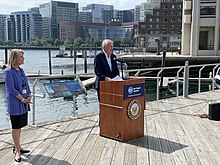 A man speaking at a podium as a woman looks on