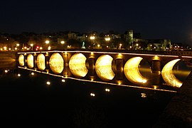 Photographie d'un pont à arches rondes éclairé la nuit.