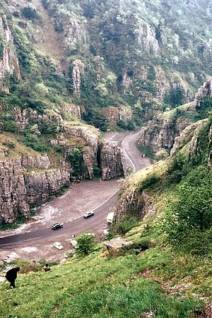 Exposed limestone cliffs on either side of a road with cars on it.