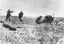 Photographie en noir et blanc d'un soldat tirant sur une femme portant un enfant, au milieu d'un champ.