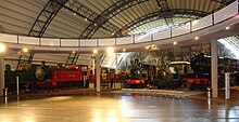 Five steam locomotives underneath a concrete walkway and a curved steel roof