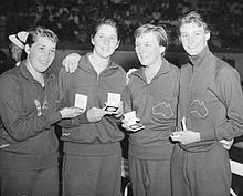 A black-and-white photograph of four young women in tracksuits holding medals in boxes