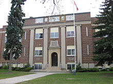 Brick three-storey building with grass and flag pole in front