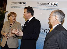 German Chancellor Angela Merkel (left), United Kingdom prime minister David Cameron (middle) and Chairman of the Munich Security Conference Wolfgang Ischinger (right) in 2011 Munich Security Conference, in Munich, Bavaria, Germany Msc2011 SZ 002 Merkel Ischinger Cameron.jpg