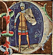 Muž s železnou helmou, drátěnou košilí a hnědou tunikou na těle. V pravé ruce drží železný oštěp, v levé pak železný štít.